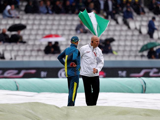 The umbrella of umpire Alex Wharf (R) is blown inside out as he stands in the rain with Australia's Nathan Lyon while covers protect the pitch. Picture: Adrian Dennis/AFP