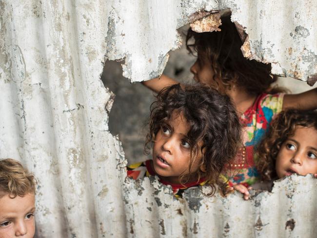 Palestinian children look through a hole in a sheet metal fence outside their home in a poor neighbourhood in Gaza City on August 8, 2017. Picture: AFP PHOTO