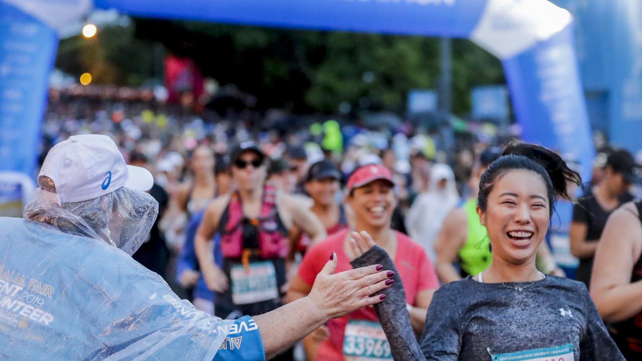 A volunteer high-fives competitors at the start of the very wet Southern Cross University 10 kilometre Run. Picture: Tim Marsden.