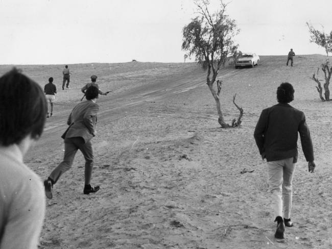 Detective Sergeant Giles (top right) fires a warning shot after Murray Brooks had tried to escape by running over a sandhill. In the foreground two Queensand police officers run toward the car, followed by reporters. Picture: Ray Titus