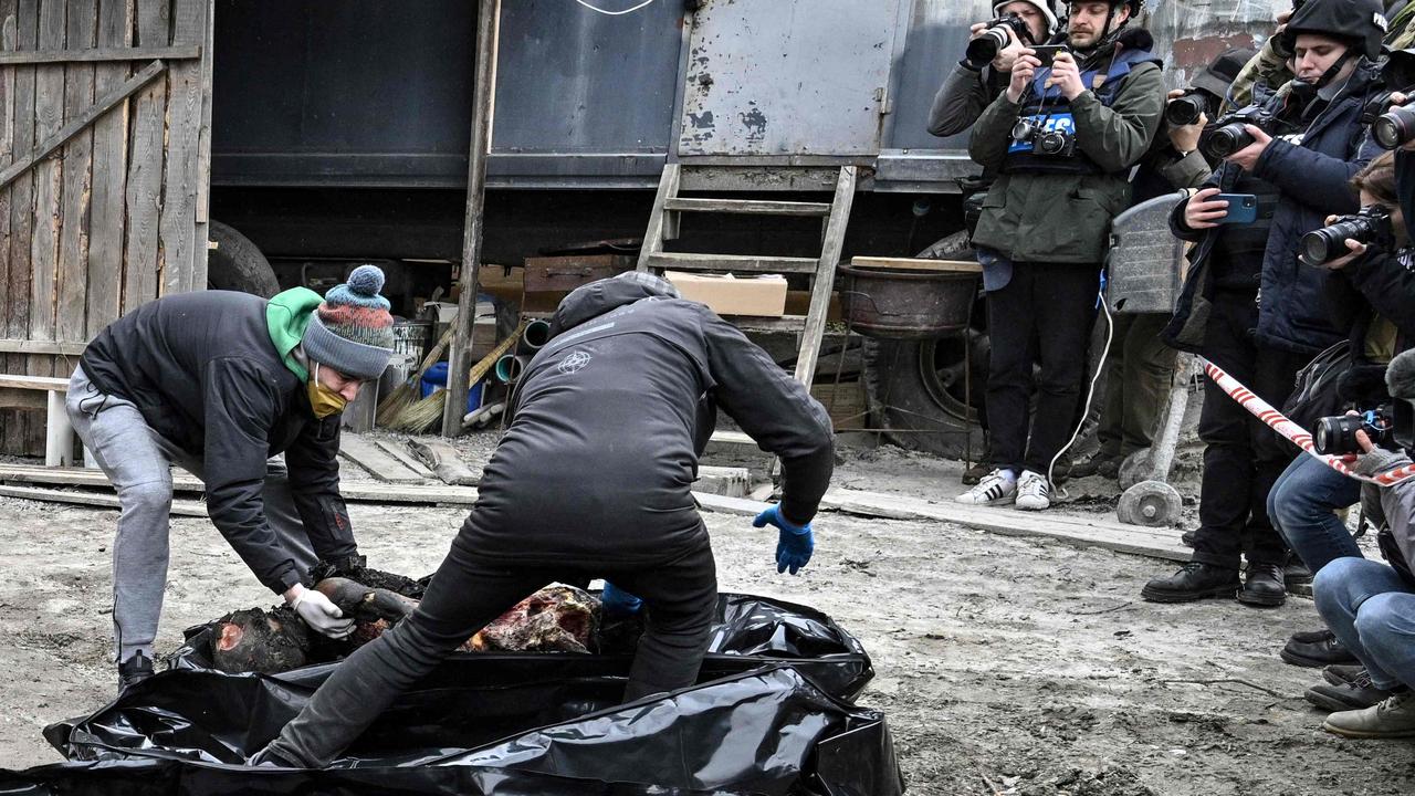 Policemen and city workers carry six partially burnt bodies into body bags as reporters attend in the town of Bucha. Picture: Genya Savilov/ AFP)