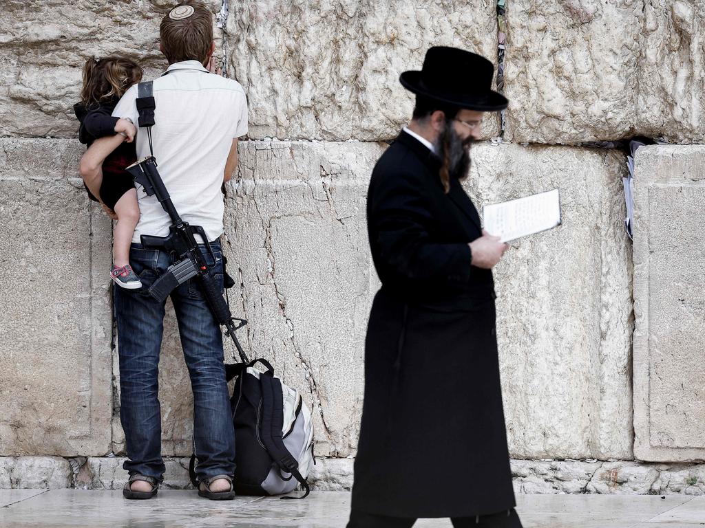 An armed Jewish man holds a child as he prays at the Western Wall, the last remaining vestige of the Second Temple, in Jerusalem's Old City. Picture: Kenzo Tribouillard/AFP