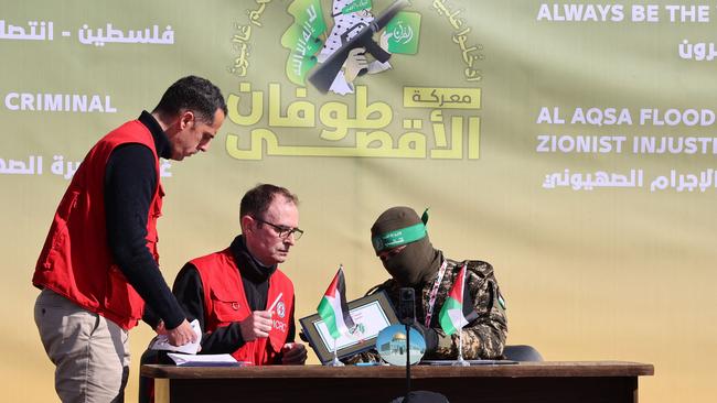 A member of a Red Cross team signs a document as Hamas fighters prepare to hand over the four Israeli hostages at a square in Gaza City. Picture: AFP