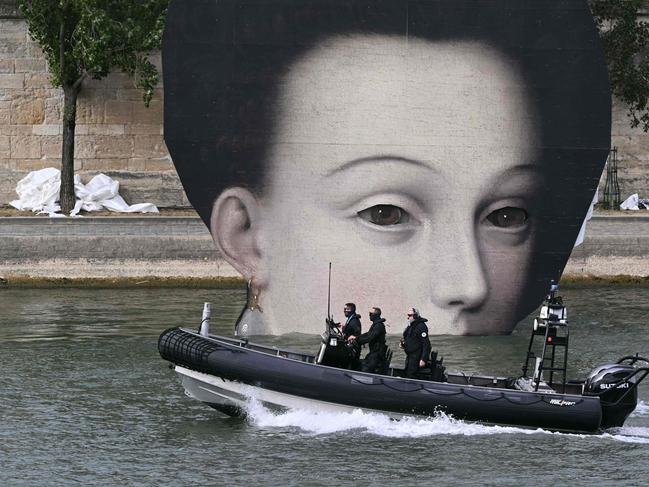 Members of police forces patrol on a boat along the Seine river next to a pannel depicting a pictorial detail ahead of the opening ceremony. Picture: Sebastien Bozon / AFP