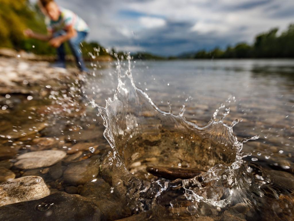 Close up of a stone splashing into water while little boy is in the background. Copy space.