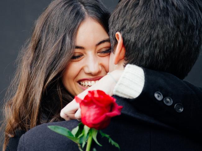 Beautiful and happy young woman in love hugging her boyfriend holding a red rose