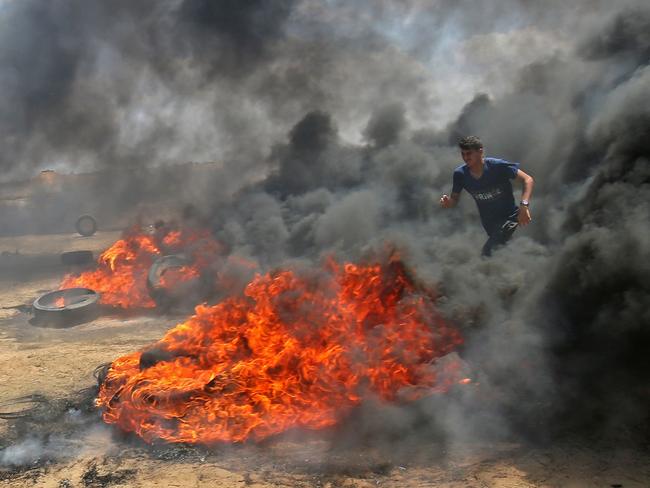 A Palestinian man walks in the smoke billowing from burning tyres during clashes with Israeli forces along the border with the Gaza Strip. Picture: AFP