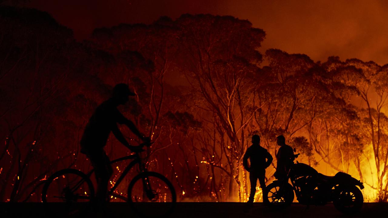 Residents look on as flames burn through bush yesterday in Lake Tabourie, in southern NSW. Picture: Brett Hemmings/Getty Images.