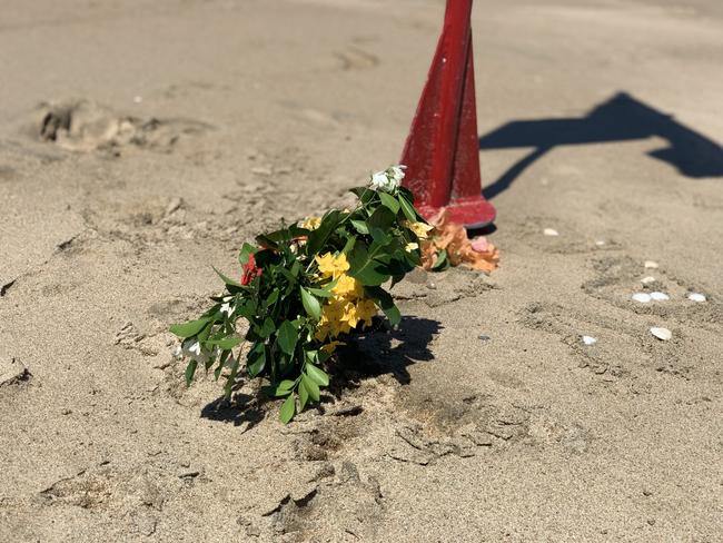 Flowers left at the base of a red flag at Eimeo Beach closed after 14-year-old boy Mark Angelo Ligmayo was stung by a box jellyfish on Saturday, February 26, 2022. He died at Mackay Base Hospital. Picture: Tara Miko