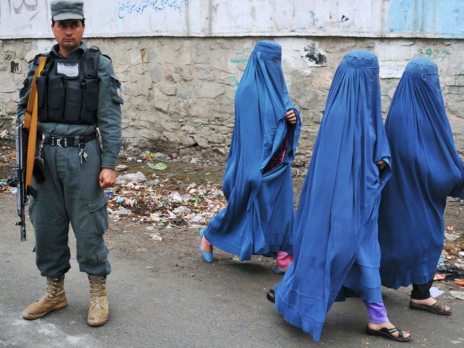 Afghan women walk past an Afghan policeman near a polling station in Jalalabad on April 5, 2014. Afghan voters went to the polls to choose a successor to President Hamid Karzai, braving Taliban threats in a landmark election held as US-led forces wind down their long intervention in the country.    AFP PHOTO/NOORULLAH SHIRZADA (Photo by Noorullah Shirzada / AFP)