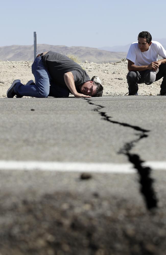 Ron Mikulaco, left, lowers his head to get a look at a crack caused by an earthquake next to his nephew Brad Fernandez on Highway 178. Picture: AP