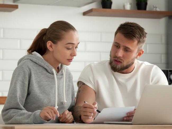 Focused young couple checking analyzing utilities bills sitting together at kitchen table, serious husband and wife reading bank loan documents with laptop, family managing finances planning expenses; money generic