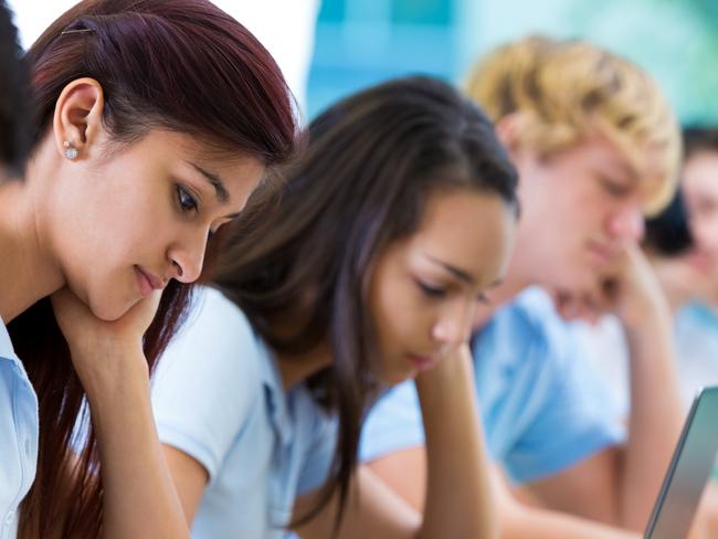 Row of private high school students work on assignment in class. They are writing or using laptops or digital tablets. They are concentrating as they study. They are wearing school uniforms. Picture: iStock