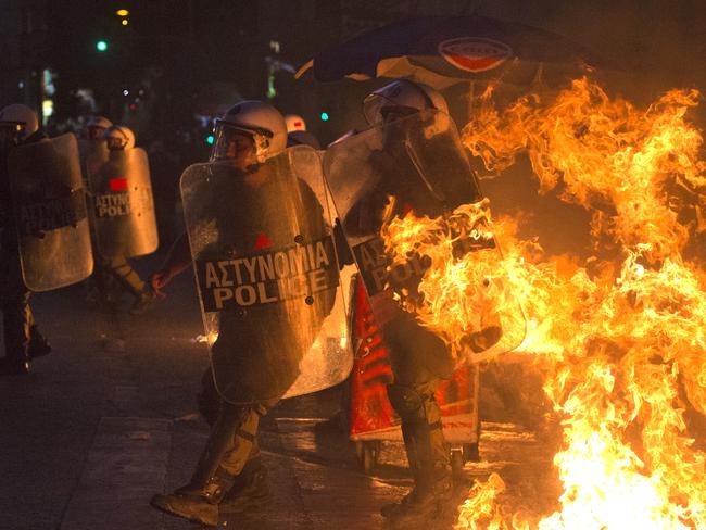 Riot police officers walk past the fire.