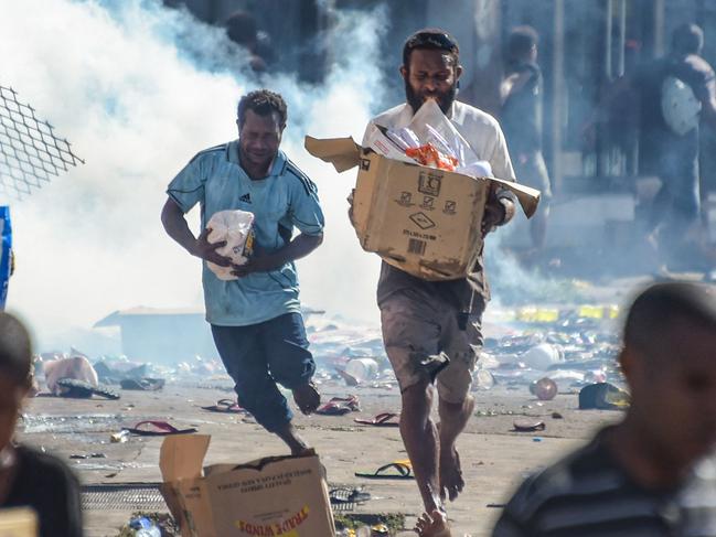 People run with merchandise as crowds leave shops with looted goods amid a state of unrest in Port Moresby on January 10, 2024. A festering pay dispute involving Papua New Guinea's security forces on January 10 sparked angry protests in the capital, where a crowd torched a police car outside the prime minister's office. By Wednesday afternoon pockets of unrest had spread through the capital Port Moresby, with video clips on social media showing crowds looting shops and stretched police scrambling to restore order. (Photo by AFP)