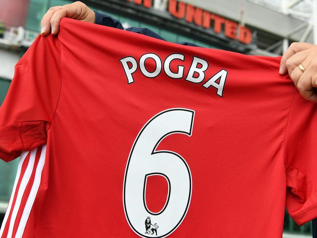 A man poses for pictures after purchasing a Manchester United shirt with the name and squad number of recent signing French midfielder Paul Pogba outside Old Traford in Manchester, north west England, on August 9, 2016. The world record for a transfer fee was shredded Tuesday when French superstar Paul Pogba completed a sensational return to Manchester United from Juventus for 105 million euros ($116 million). / AFP PHOTO / PAUL ELLIS