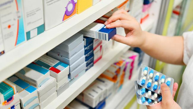 Pharmacist holding medicine box and capsule pack in pharmacy drugstore.