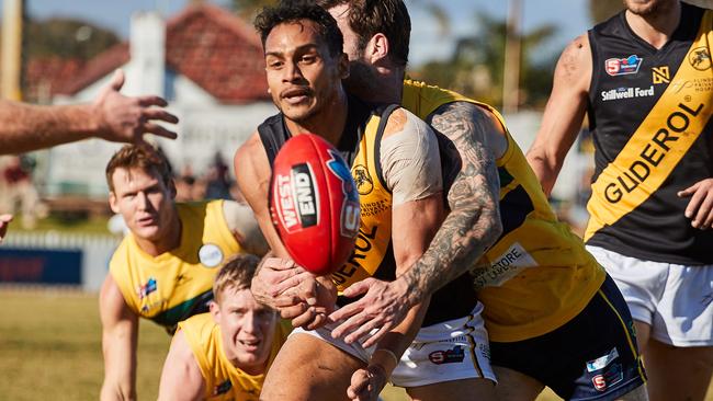 Glenelg's Marlon Motlop handpasses under pressure from Eagle Jack Firns. Picture: MATT LOXTON