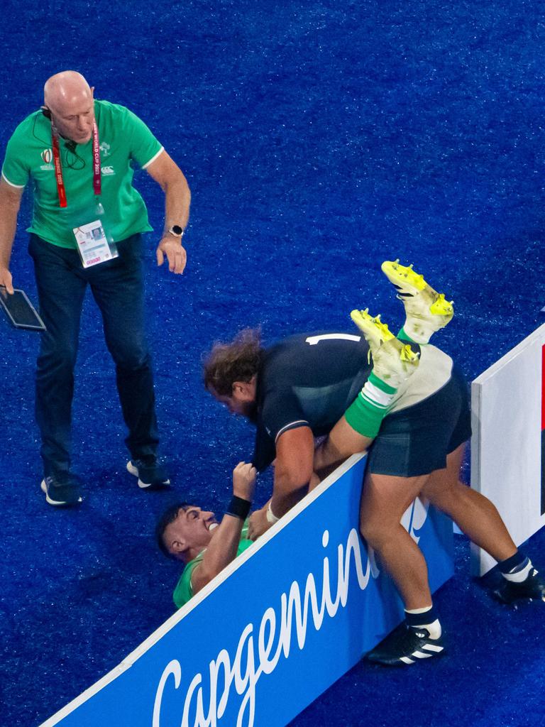 An official (L) looks on as Scotland's loosehead prop Pierre Schoeman (R) and Ireland's hooker Dan Sheehan tussle across an advertising hoarding. (Photo by FranÃ§ois-Xavier MARIT / AFP)