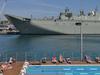 People sunbath at a swimming pool in front of HMAS Canberra, the Royal Australian Navy's latest warship, which is berthed at Garden Island naval base in Sydney on November 21, 2014. HMAS Canberra is the Royal Australian Navy's largest and most expensive warship and will be commissioned into service on November 28, 2014. AFP PHOTO/Peter PARKS