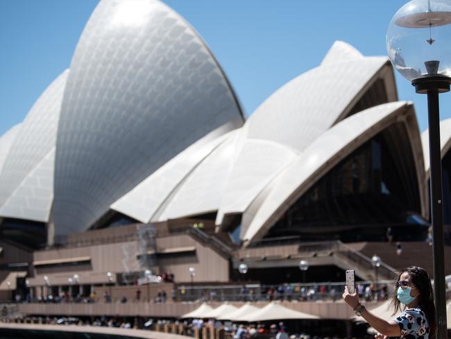 A woman takes a selfie whilst wearing a protective face mask in front of the Sydney Opera House, Sydney, Friday, March 13, 2020. NSW is ramping up efforts to contain the spread of COVID-19 virus, with fears as many as 1.6 million could be infected if the pace of the outbreak continues. (AAP Image/James Gourley) NO ARCHIVING