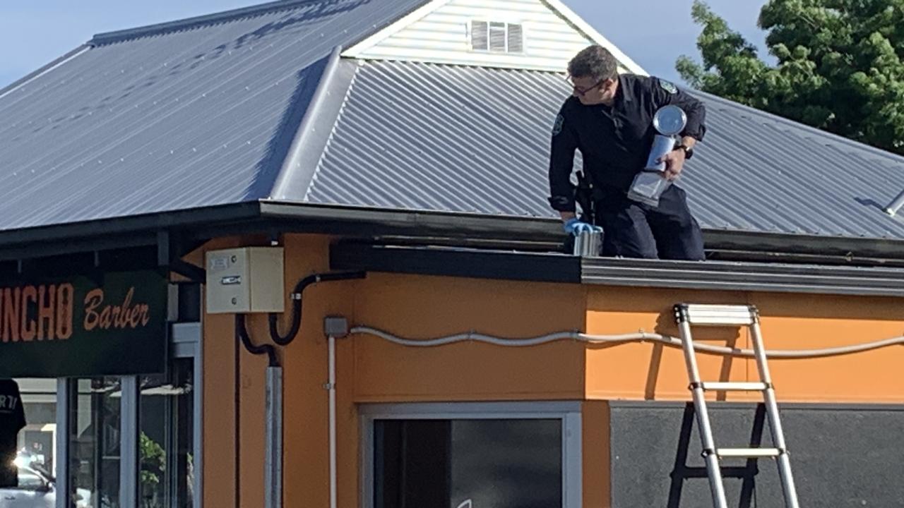 Crime scene investigators pictured on the roof examining a crawl space above the barber shop. Picture: George Yankovich