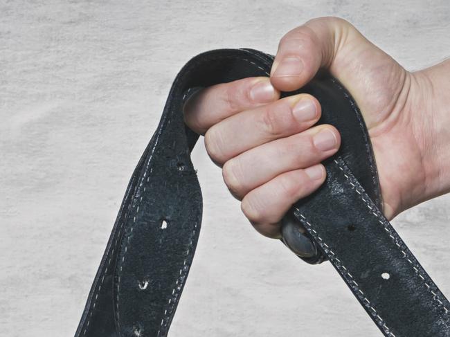 Hand holds leather belt for punishment. Family violence concept.