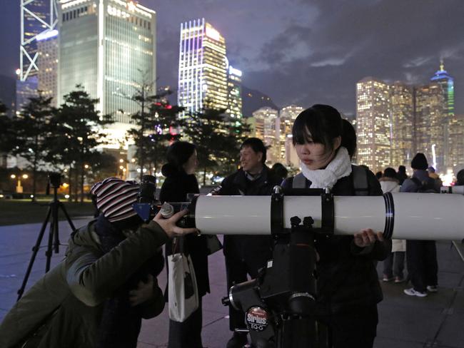 Hong Kong stargazers use telescopes to observe the moon along Victoria Habour. Picture: AP/Kin Cheung