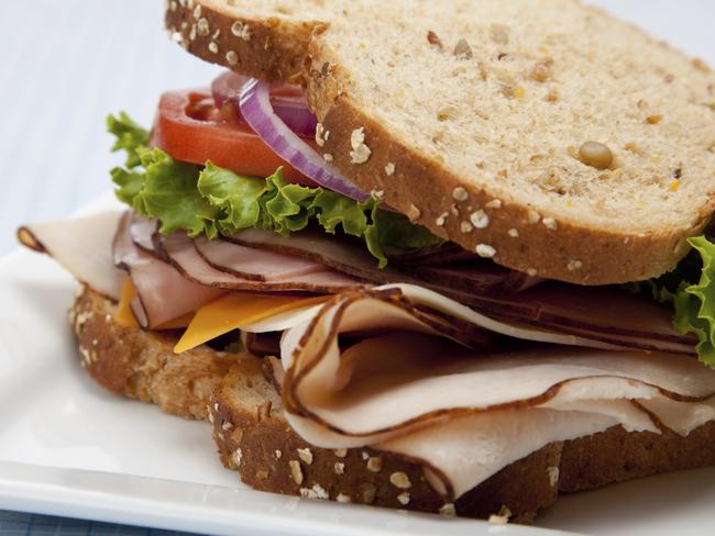 A turkey sandwich with turkey, lettuce, onion, tomato and cheese on whole grain bread on a white background