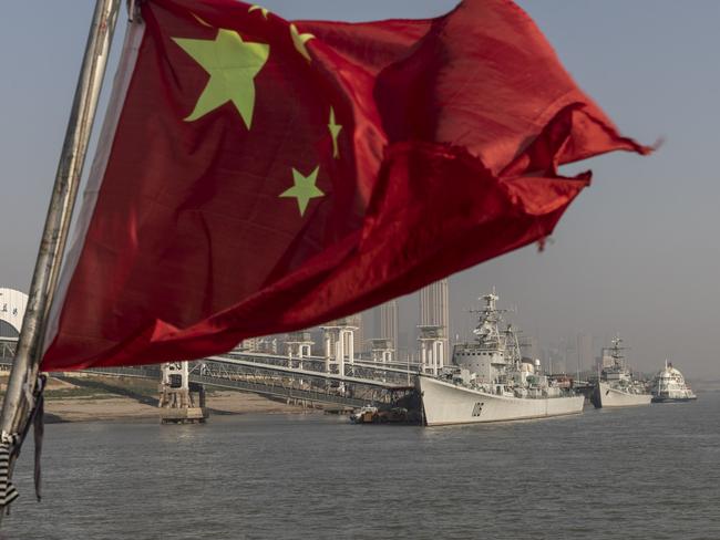 A Chinese national flag flies from a ferry as the retired People's Liberation Army (PLA) Navy Xian frigate ship, from left, and the Huaian frigate ship sit anchored on the Yangtze River in Wuhan, Hubei, China, on Wednesday, Dec. 11, 2019. China's economic growth will come in at 5.9% in 2020 as easing trade tensions and the prospect of lower bank borrowing costs boost confidence, according to analysts and traders. Photographer: Qilai Shen/Bloomberg