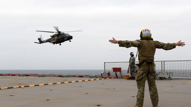 Flight marshals on the HMAS Choules signalling to a helicopter as the navy provides support to the communities affected by bushfires in New South Wales. Picture: Helen Frank/Royal Australian Navy