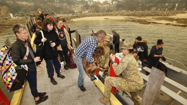 Mallacoota resdidents are loaded onto landing boats by ADF personal after fire tore through the town. Picture: David Caird