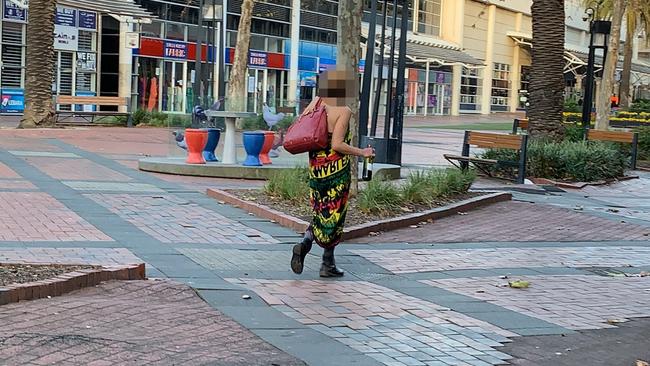 A woman walks along a Dandenong main street with a bottle of booze in her hand.