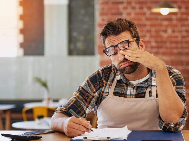 CAREERS: exhausted young business owner doing admin at a table in his coffee shopStressed cafe owner.Picture: iStock