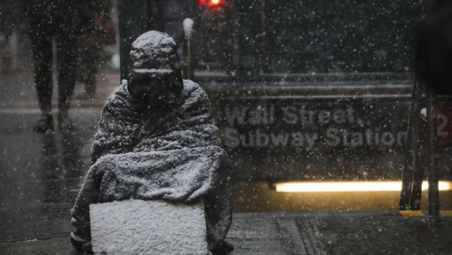 A homeless man covered in snow tries to sleep outside a subway station in New York. Picture: Getty Images