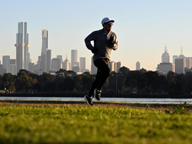 With the Melbourne skyline in the background, a jogger takes part in an early morning fun run around Albert Park Lake as Melbourne awoke to freezing conditions on July 3, 2024. (Photo by William WEST / AFP)