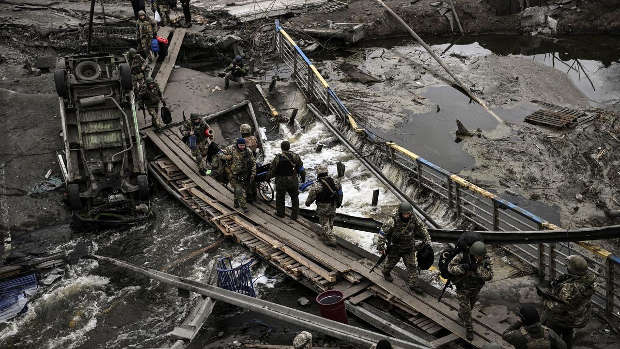 Ukrainian servicemen walk on a makeshift pathway to cross a river next to a destroyed bridge near the city of Irpin, northwest of Kyiv. Picture: AFP