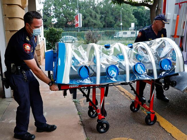 City of Tshwane's Special Infection Unit Leading Emergency Care Practitioner Rocco Veer (L) and Station Officer Arrie Visser (R) push the isolation chamber equipped with a negative pressure filtration system used to transport positive Covid-19 patients before starting their night shift at the Hatfield Emergency Station, in Pretoria, on December 28, 2020. (Photo by Phill Magakoe / AFP)