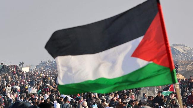 A person waves a Palestinian flag as people walk along Gaza's coastal al-Rashid Street to cross the Netzarim corridor from the southern Gaza Strip into the north on January 27, 2025. Displaced Palestinians began returning to northern Gaza on January 27, an official at the territory's Hamas-run Interior Ministry told AFP, after a breakthrough in negotiations between Hamas and Israel. (Photo by Omar AL-QATTAA / AFP)