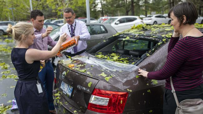 Eleanor Goodwin, right, receives help from bystanders to cover her car with cling wrap after it was damaged during a hailstorm. Picture: Sean Davey.