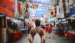 Rear view image of a young man, solo traveler, walking in the Chinatown district of Kuala Lumpur, Malaysia. He is wearing a white rucksack, enjoying walking and shopping in Malaysia capital.