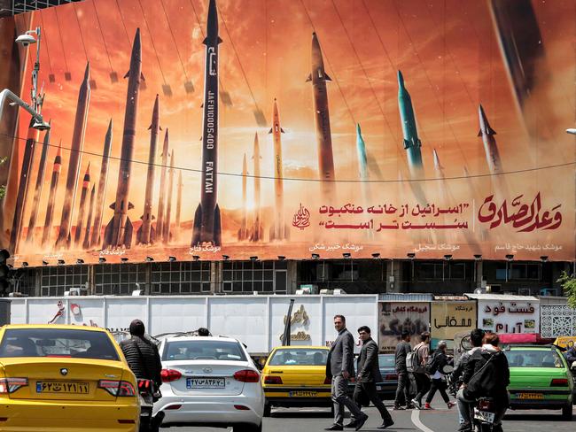 TOPSHOT - Motorists drive their vehicles past a billboard depicting named Iranian ballistic missiles in service, with text in Arabic reading "the honest [person's] promise" and in Persian "Israel is weaker than a spider's web", in Valiasr Square in central Tehran on April 15, 2024. Iran on April 14 urged Israel not to retaliate militarily to an unprecedented attack overnight, which Tehran presented as a justified response to a deadly strike on its consulate building in Damascus. (Photo by ATTA KENARE / AFP)