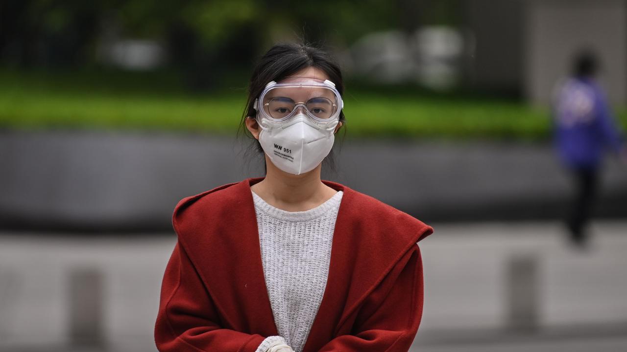 A woman wearing a facemask and googles walks along a street in Wuhan in China’s central Hubei province on April 5, 2020. (Photo by Hector RETAMAL / AFP)