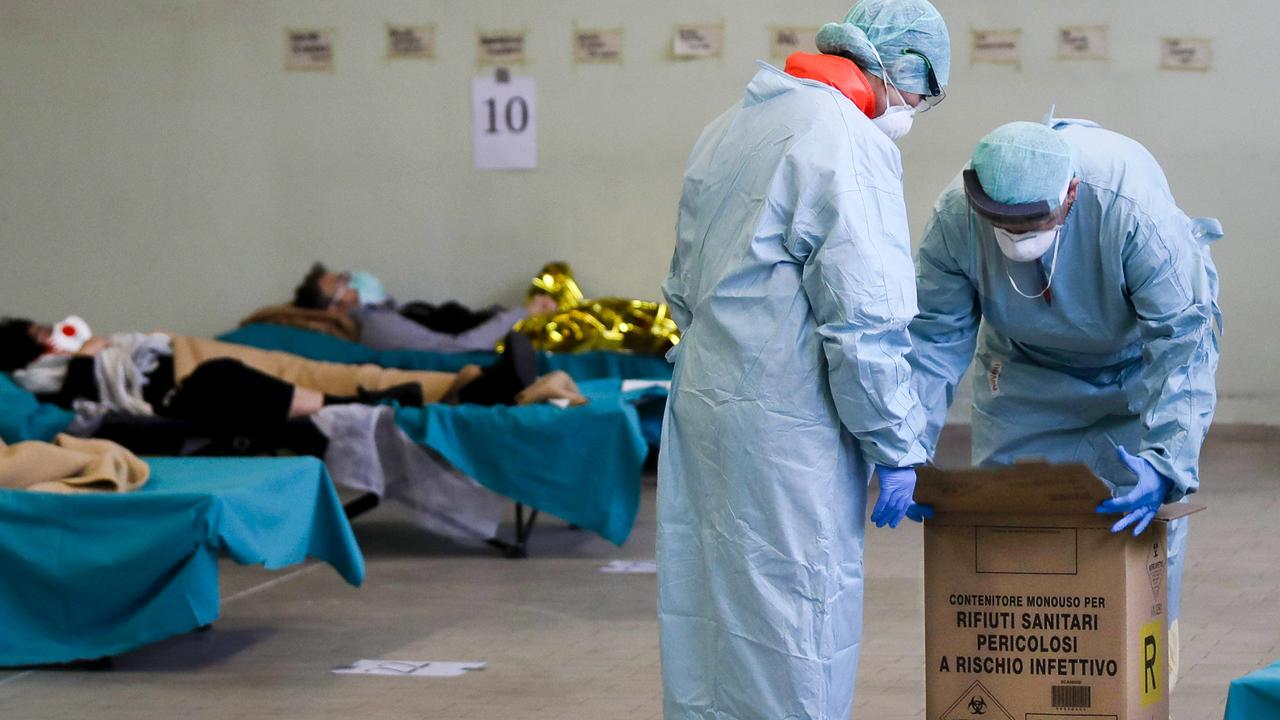 Paramedics carry a hazardous medical waste box as patients lie on camp beds in one of the emergency structures that were set up to ease procedures at the Brescia hospital, northern Italy. Picture: Luca Bruno/AP