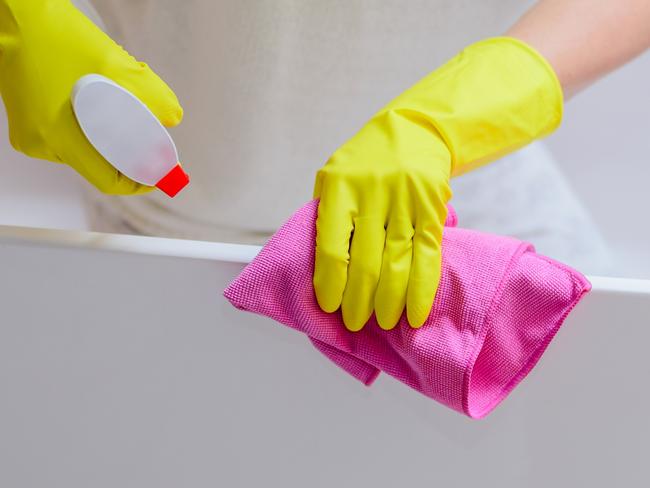 Female hands with yellow rubber protective gloves cleaning bath with pink cloth and spray detergent. Spring cleaning