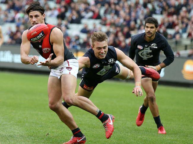 Essendon's Mark Baguley handballs as he is tackled by Carlton's Patrick Cripps. Picture: Michael Klein