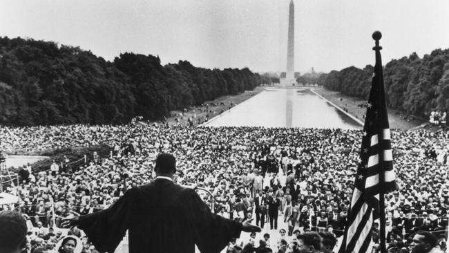 Martin Luther King, Jr. dressed in black robes and holding out his hands towards the thousands of people who have gathered to hear him speak near the Reflecting Pool in Washington, DC during the Prayer Pilgrimage.