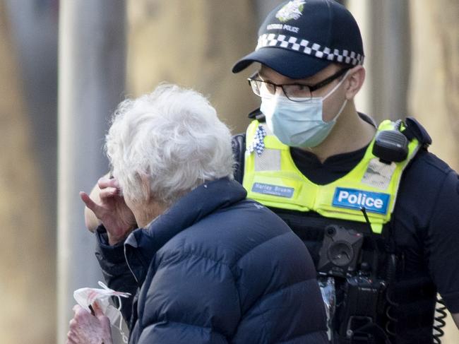 A police officer helps an elderly woman put on a face mask in Melbourne’s CBD. Picture: David Geraghty