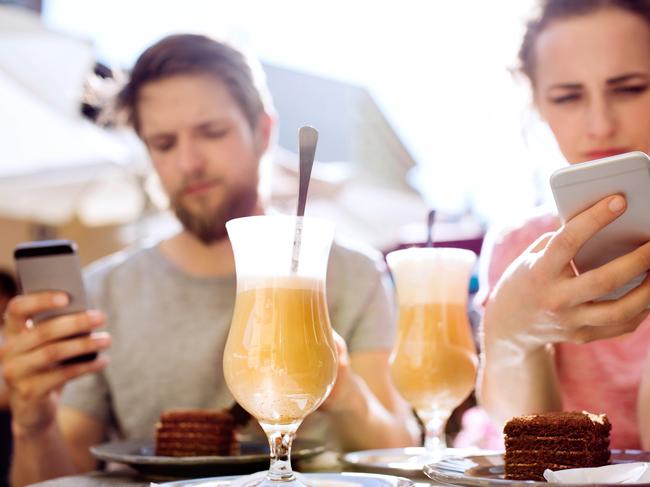 Beautiful young couple with smart phones sitting in cafe, watching or reading something. Sunny spring day.