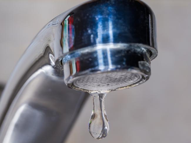 Drop of water from the outlet of leaking mixer tap with aerator on a blurred background, close-up in selective focus